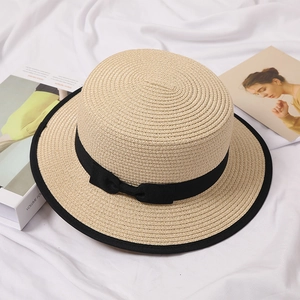 Detailed close-up of a white boater hat with a black ribbon bow on white fabric