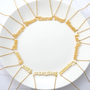 Flat lay of twelve gold zodiac necklaces with gothic lettering on white ceramic plate