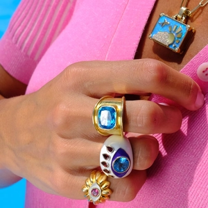 Macro detail of gold-plated rings with blue gemstones and enamel on a model's hand