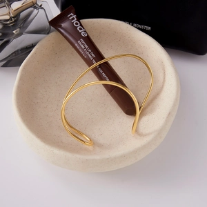 Detail of a minimalist gold-plated open bangle with a sleek double-line crossover design