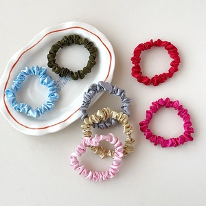Flat lay of colorful satin silk scrunchies in diverse colors on a white ceramic plate
