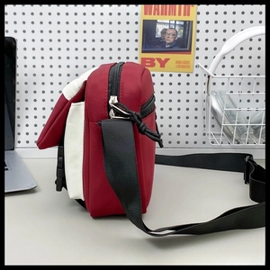 Detail view of red and white nylon crossbody bag with black strap and buckle closure