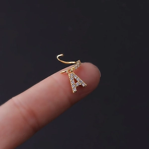 Close-up of golden letter A nose ring with micro-pave cubic zirconia on a black background