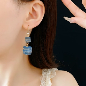 Close-up of blue geometric square drop earrings with gold stripes worn by a model