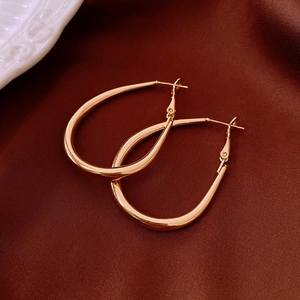 Detailed close-up of shiny gold-plated oval hoop earrings on dark red satin fabric
