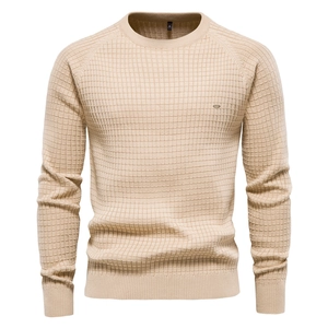 Gros plan sur la maille gaufrée beige avec un petit logo métallique détaillé sur la poitrine