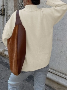 Dettaglio di un maglione beige a collo alto con polsini a coste e borsa a tracolla marrone