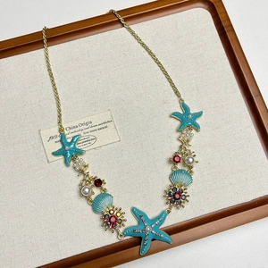 Detail of starfish enamel charms with faux pearls and red gems on a gold chain