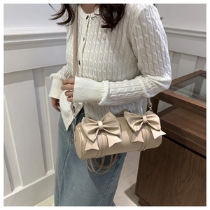 Detailed view of beige cylindrical shoulder bag featuring three large bows and silver hardware