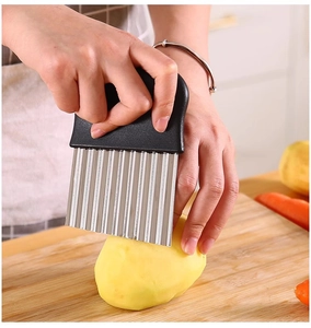 Action shot of stainless steel crinkle cutter slicing a potato on a wooden board
