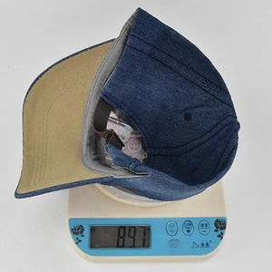 Dettaglio del cappellino in denim blu che mostra il peso di 89,7g sulla bilancia