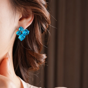 Close-up of blue crystal cube earrings with a multi-layered geometric design on model