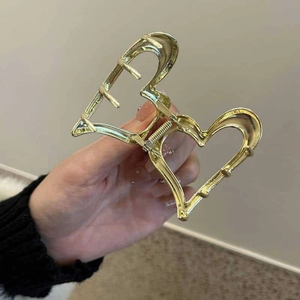 Close-up of a golden heart-shaped metal hair claw clip being held by hand