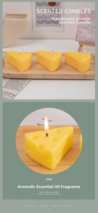Close-up of cheese-shaped scented candles on a wooden tray with a warm glowing wick