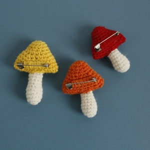 Handmade crochet mushroom brooches in yellow, orange, and red yarn on a blue background