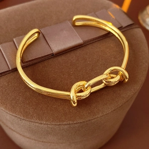 Detail of gold knot open cuff bracelet displayed on dark brown velvet jewelry box