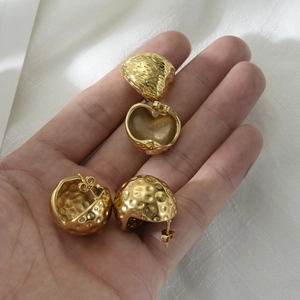 Textured gold dome earrings with hammered finish held in hand on silk background