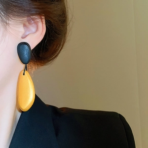 Close-up of irregular wood drop earrings in black and yellow on a female model