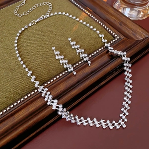 Detailed view of silver square rhinestone necklace and earring set on green fabric base