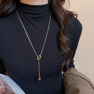 Detail of tiger eye stone pendant on golden snake chain worn over a black sweater