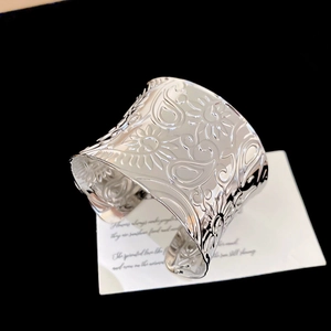 Detailed view of silver paisley and sunflower embossed patterns on a wide cuff bracelet