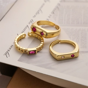 Detailed close-up of three gold open rings with red and clear zircon stones on a book