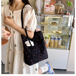 Close-up of black corduroy bucket bag with red strawberry patterns and plush charm