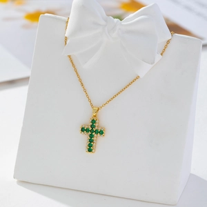 Detail of gold cross pendant necklace featuring green and white cubic zirconia stones