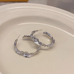 Minimalist silver irregular C-shaped earrings with liquid metal texture on ceramic tray