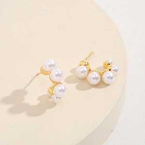 Elegant gold-tone pearl earrings in a curved design on a minimalist display stand