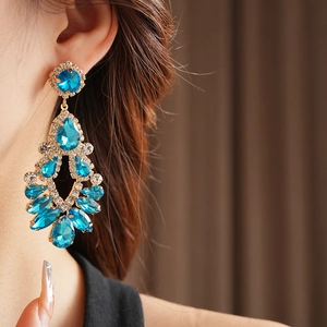 Macro view of gold chandelier earrings with blue teardrop stones and rhinestones on model