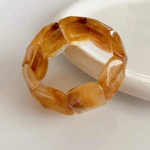 Detail shot of warm amber resin beads on an elastic bracelet against white porcelain