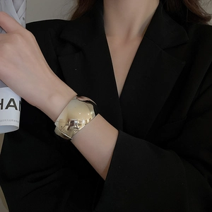Close-up of a wide polished silver cuff bracelet on a model wearing a black blazer