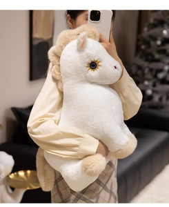 Close-up of soft white plush horse toy with beige mane held by a person in a cozy room
