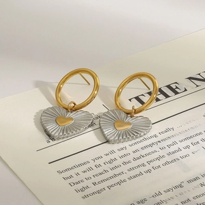 Elegant two-tone stainless steel hoop earrings with heart charms on newspaper background