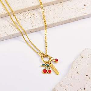 Detail of gold necklace featuring enamel cherry, AMOUR bar, and red stone charm