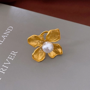 Close-up of golden floral open ring with brushed metal texture and large white pearl