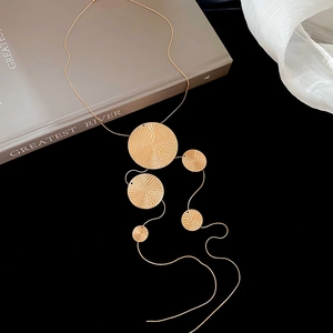 Détail de cinq disques métalliques dorés texturés sur une longue chaîne de pull chic