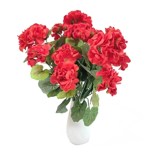 Detail of red artificial geranium flower cluster with textured green leaves in white vase