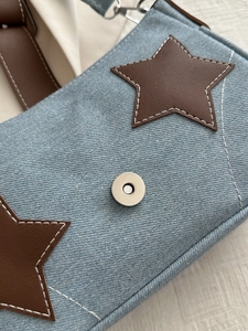 Close-up of blue denim handbag with brown leather star patch and silver magnetic buckle