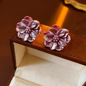 Vue macro de boucles d'oreilles fleur en résine prune sur un écrin en cuir brun