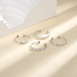 Detailed view of four silver open rings set with elegant white pearls on a minimalist background
