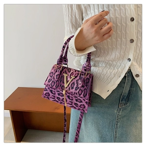 Dettaglio borsa leopardata viola con fibbia a V dorata tenuta da una modella