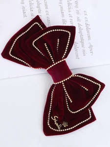 Detail of burgundy velvet hair bow with gold beaded edges and elegant metal accents