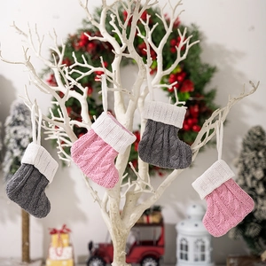 Pink and grey knitted Christmas stockings with white cuffs hanging on a festive tree