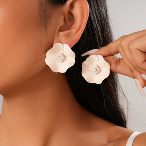 Minimalist cream flower stud earrings with a crystal center on a model's ear