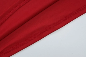 Detailed close-up of red knit fabric showing professional overlock stitching and hem