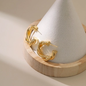 Detailed view of gold twisted C-shape earrings displayed on a minimalist wooden jewelry stand
