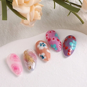 Pink blush gradient nail tips with floral patterns and gold leaf accents on a marble base