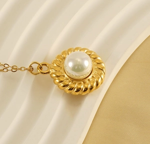 Detail of 18k gold plated necklace featuring a textured spiral frame and large pearl pendant